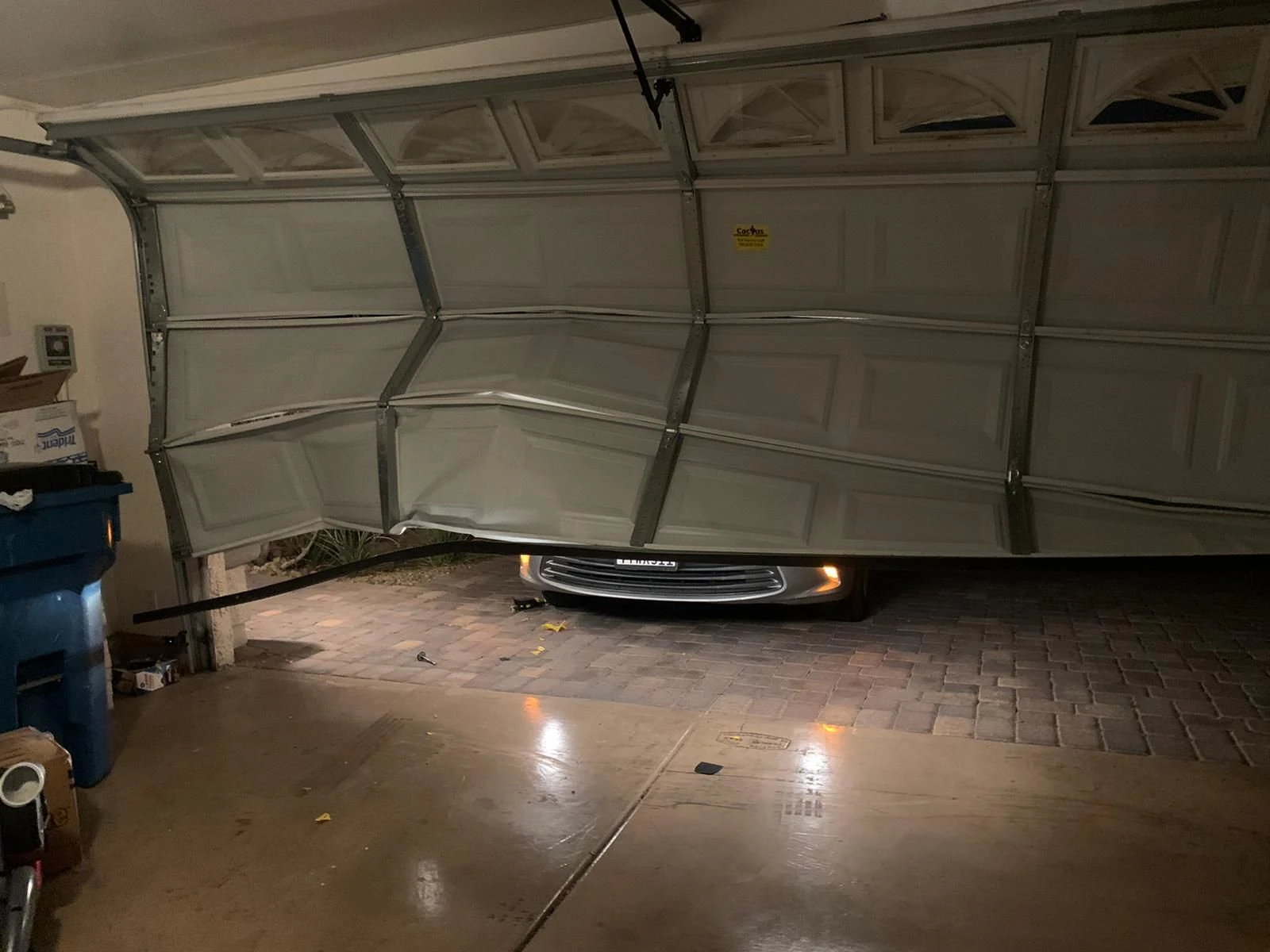 Garage door with several buckled and bent sections seen from inside a Las Vegas garage at night