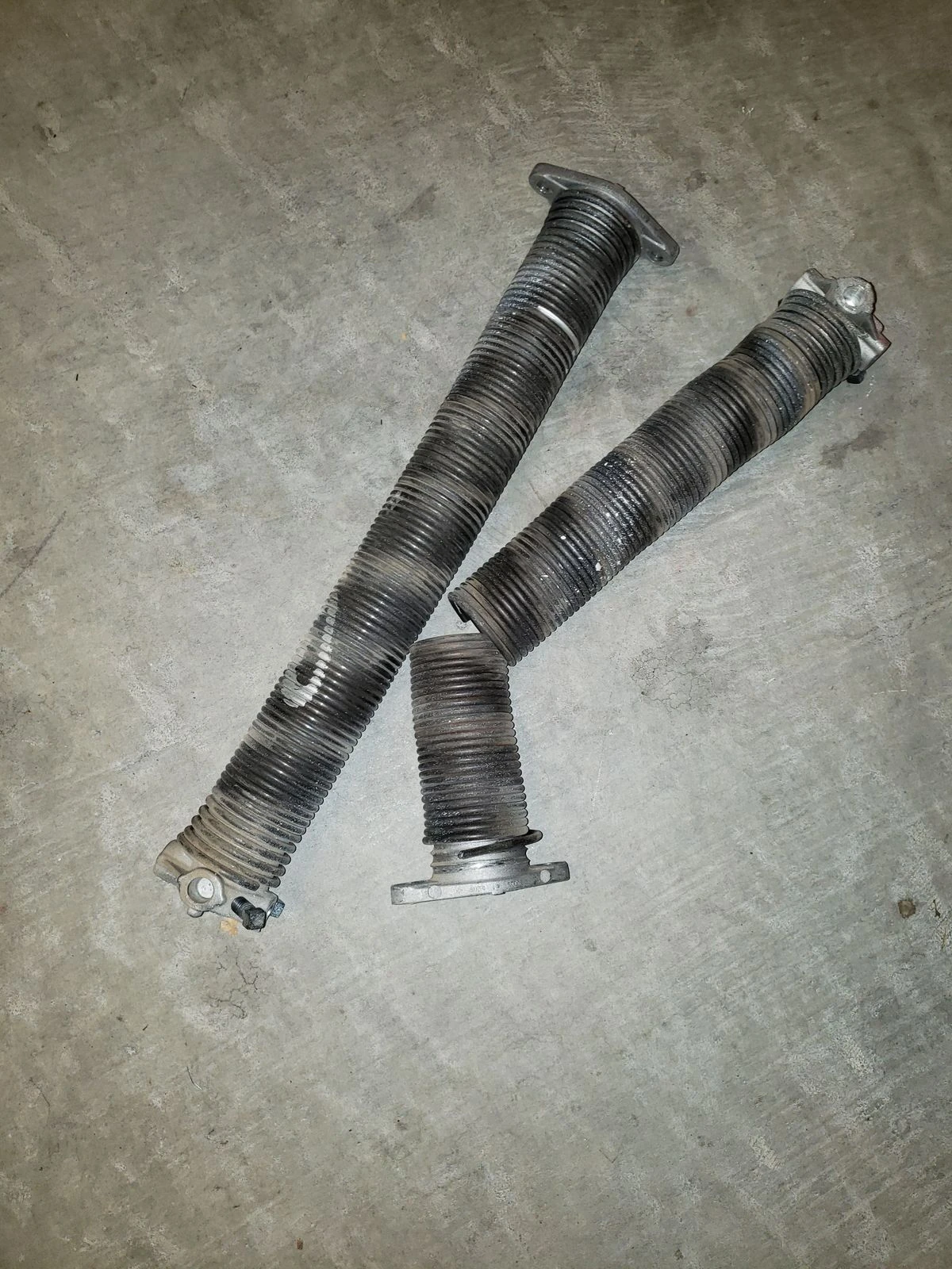 Two old torsion springs on a garage floor after removal, one snapped clean in two